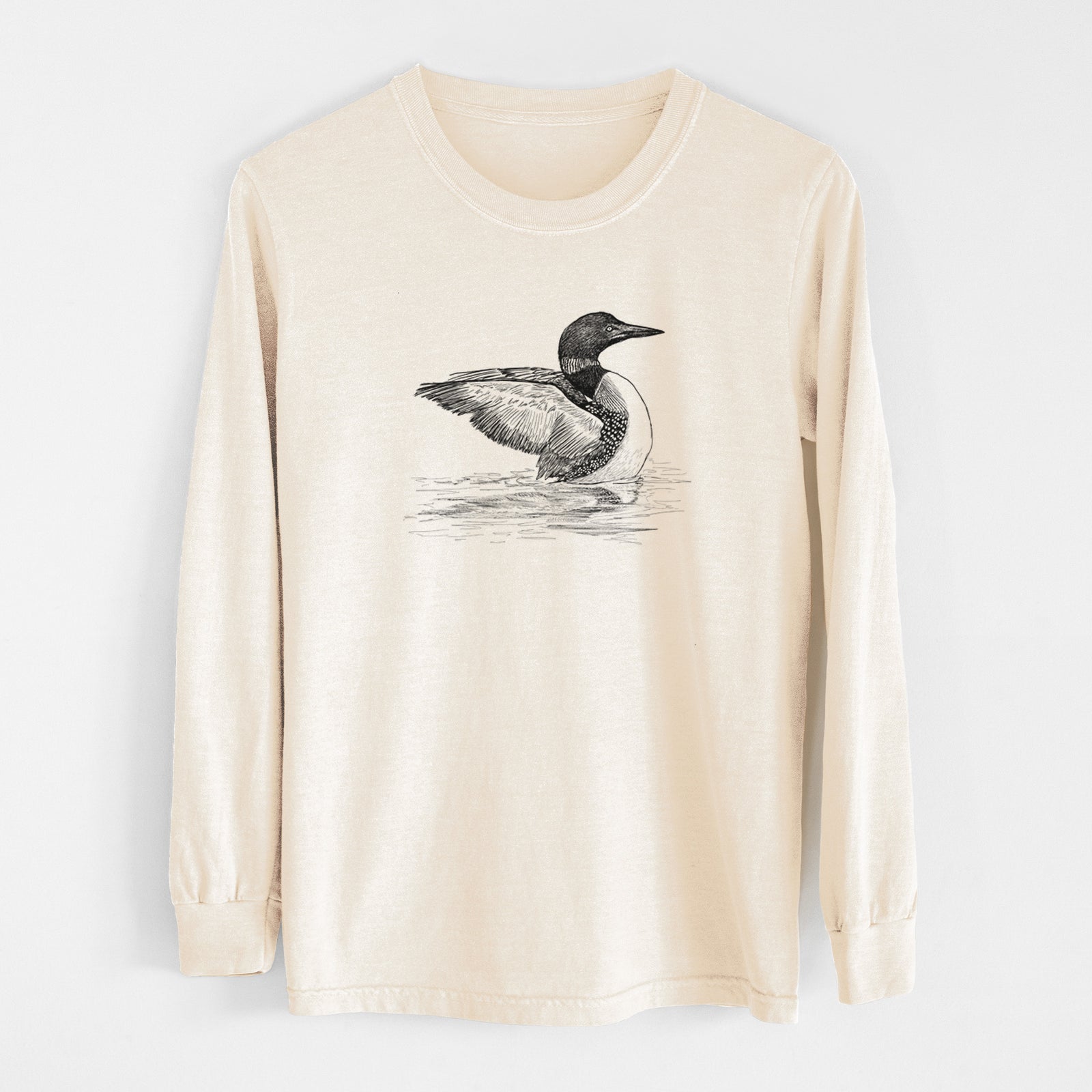 Ivory Comfort Colors long sleeve shirt laid flat, printed with a detailed black ink sketch of a common loon floating on rippling water.