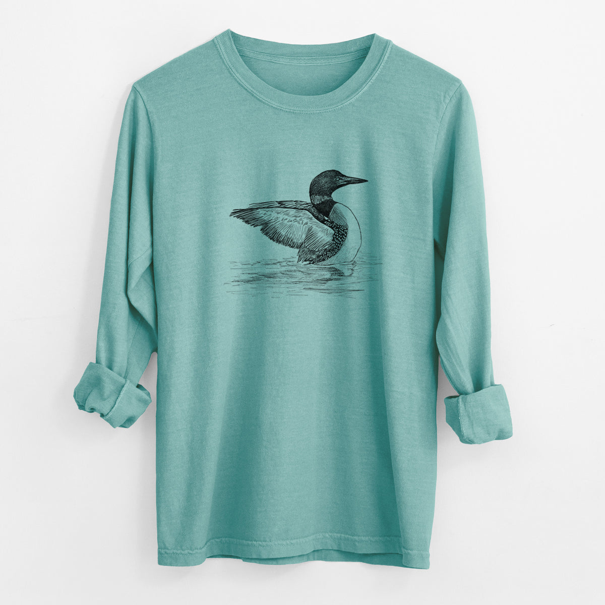 Reef green Comfort Colors long sleeve shirt laid flat with the cuffs rolled, printed with a detailed black ink sketch of a common loon floating on rippling water.