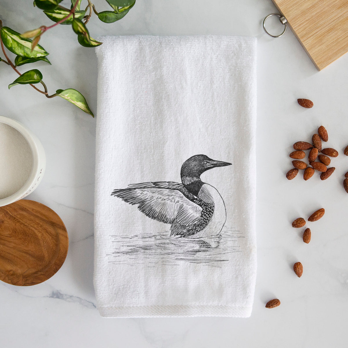 White hand towel printed with a detailed black ink sketch of a common loon floating on rippling water.
