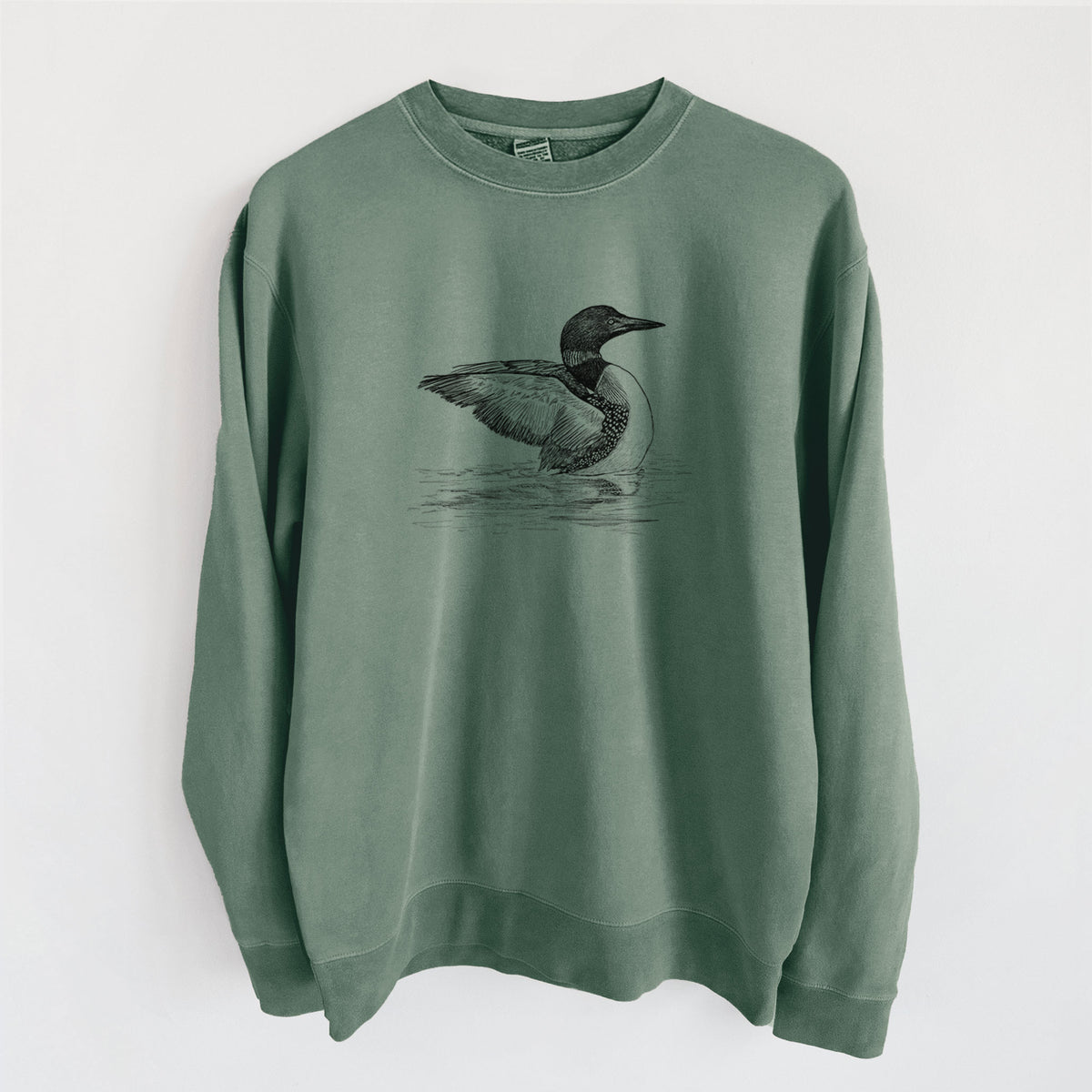 Alpine green pigment dyed crewneck sweatshirt laid flat, printed with a detailed black ink sketch of a common loon floating on rippling water.