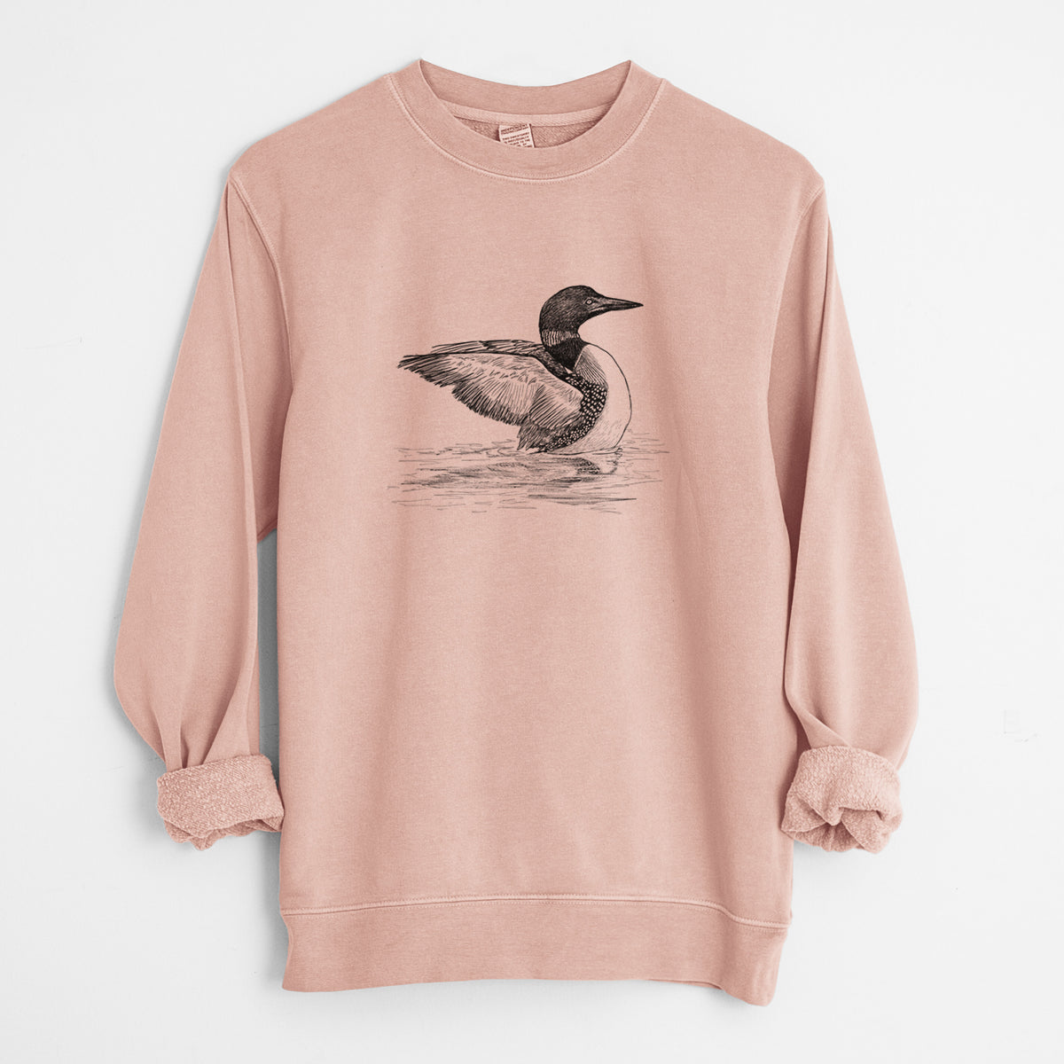 Dusty pink pigment dyed crewneck sweatshirt laid flat with the sleeves rolled, printed with a detailed black ink sketch of a common loon floating on rippling water.