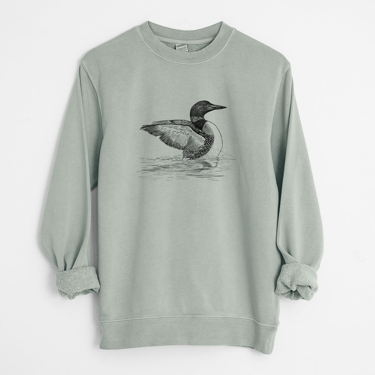 Sage green pigment dyed crewneck sweatshirt laid flat with the sleeves rolled, printed with a detailed black ink sketch of a common loon floating on rippling water.