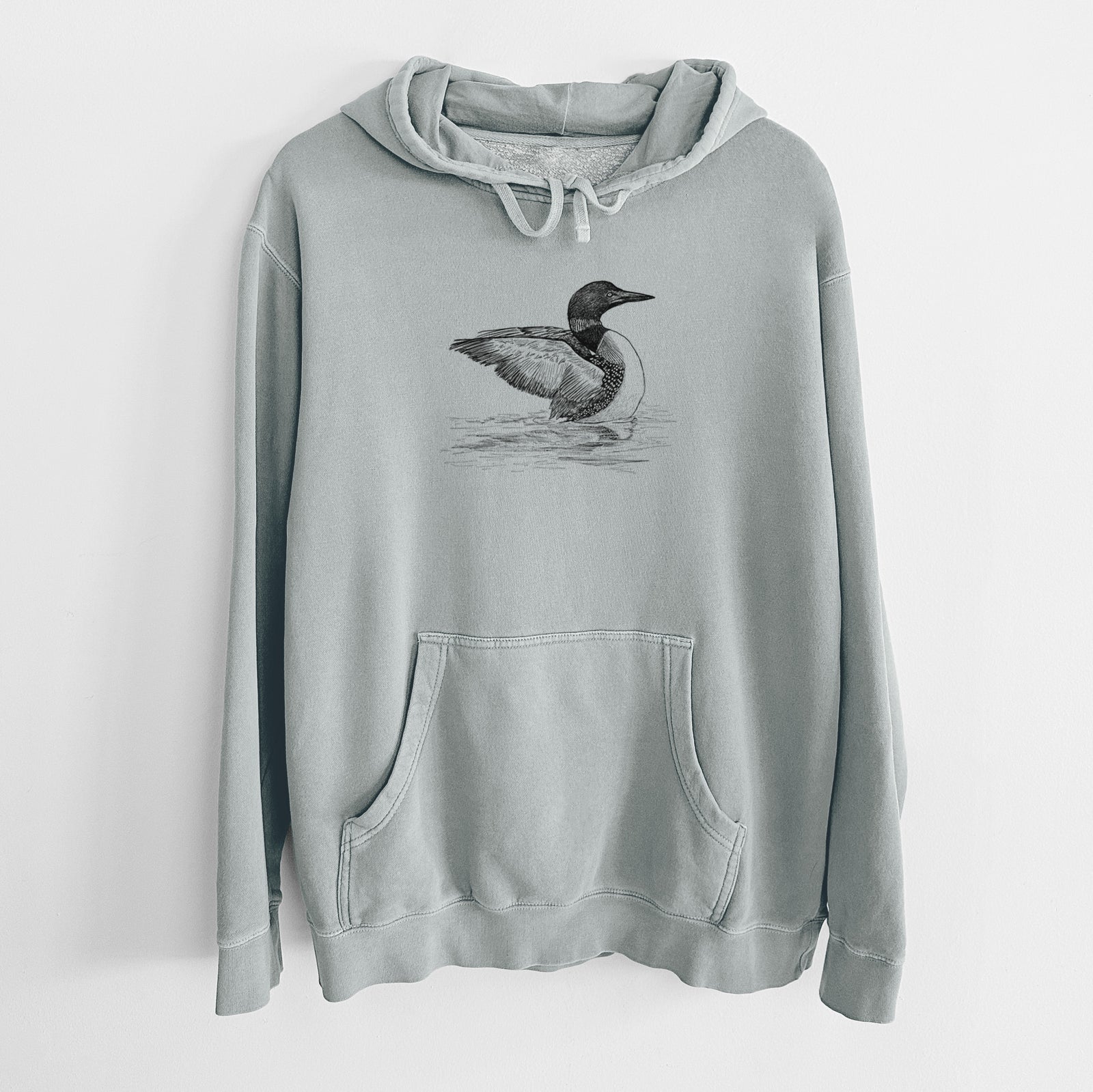 Sage green pigment dyed hoodie laid flat, printed with a detailed black ink sketch of a common loon floating on rippling water.