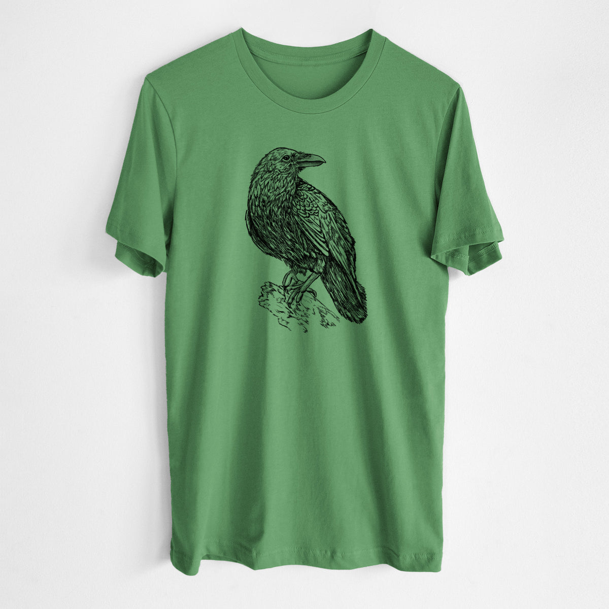 Leaf green lightweight cotton t-shirt laid flat, printed with a detailed black ink sketch of a common raven perched on a rock.