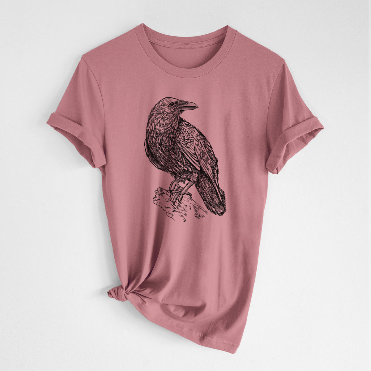 Mauve pink lightweight cotton t-shirt laid flat with the sleeves rolled, printed with a detailed black ink sketch of a common raven perched on a rock.