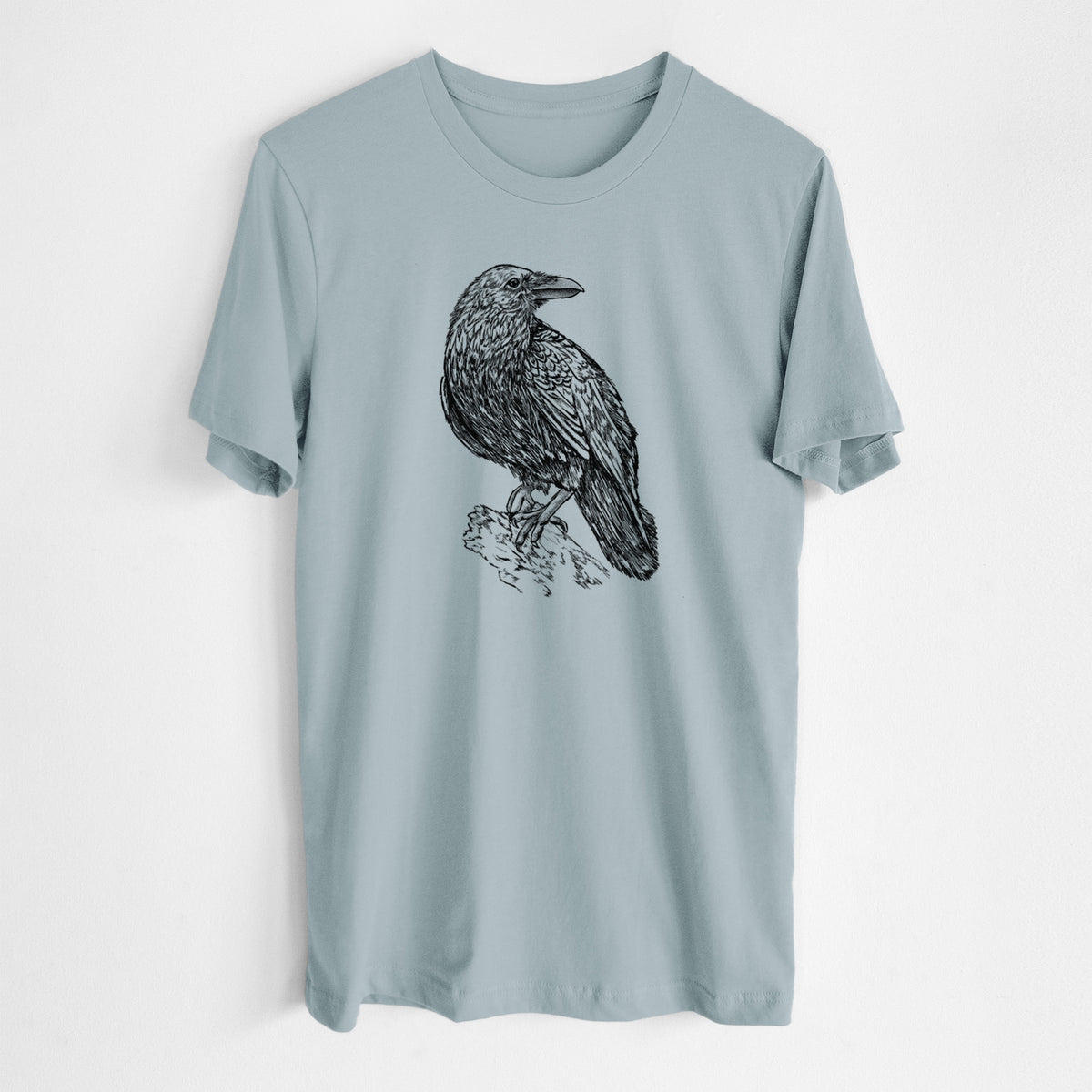 Vintage denim lightweight cotton t-shirt laid flat, printed with a detailed black ink sketch of a common raven perched on a rock.