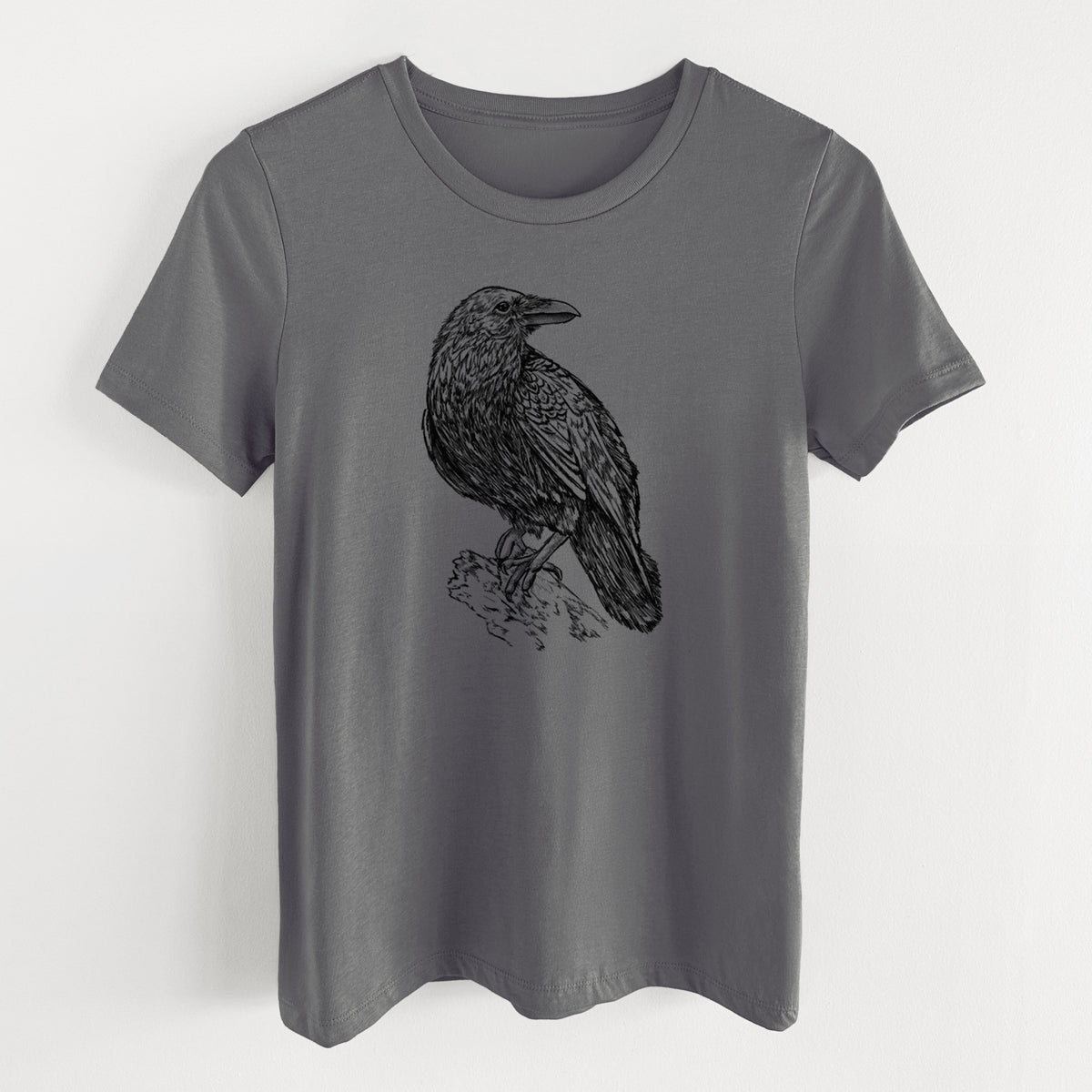 Asphalt women's relaxed fit cotton t-shirt laid flat, printed with a detailed black ink sketch of a common raven perched on a rock.