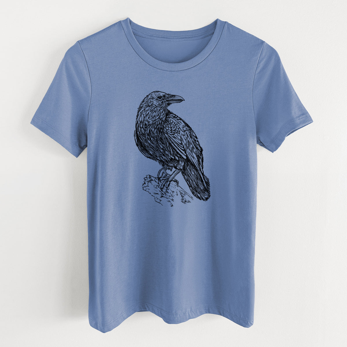 Blue bell women's relaxed fit cotton t-shirt laid flat, printed with a detailed black ink sketch of a common raven perched on a rock.