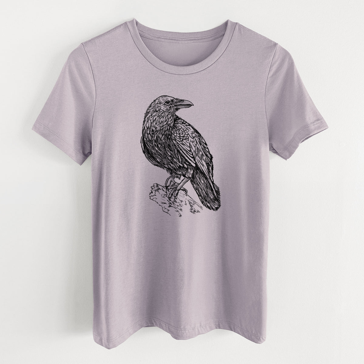 Light violet women's relaxed fit cotton t-shirt laid flat, printed with a detailed black ink sketch of a common raven perched on a rock.