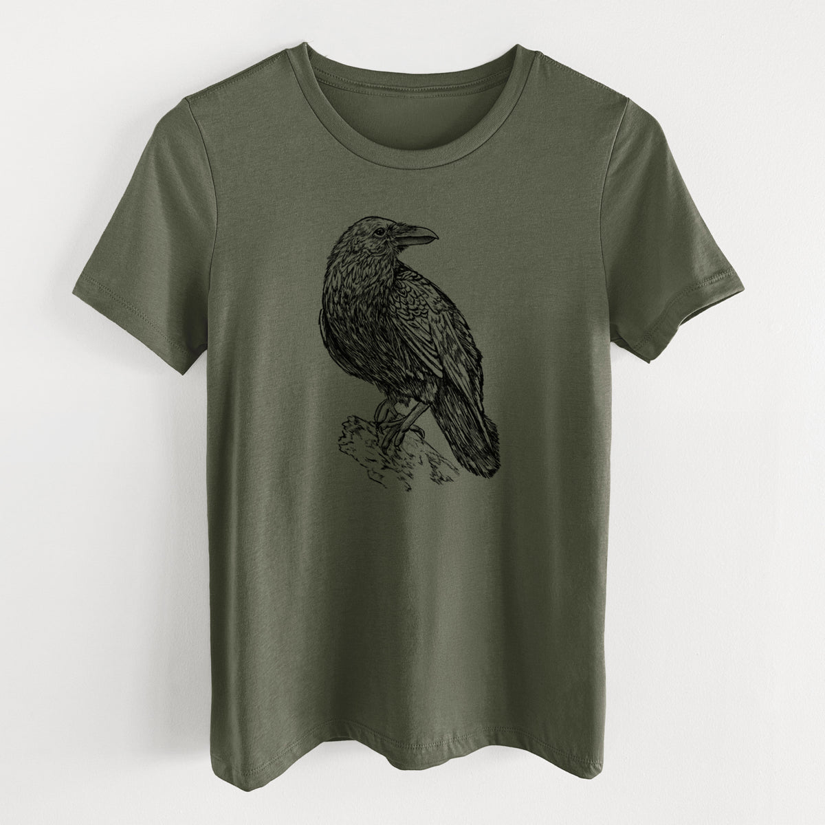 Military green women's relaxed fit cotton t-shirt laid flat, printed with a detailed black ink sketch of a common raven perched on a rock.