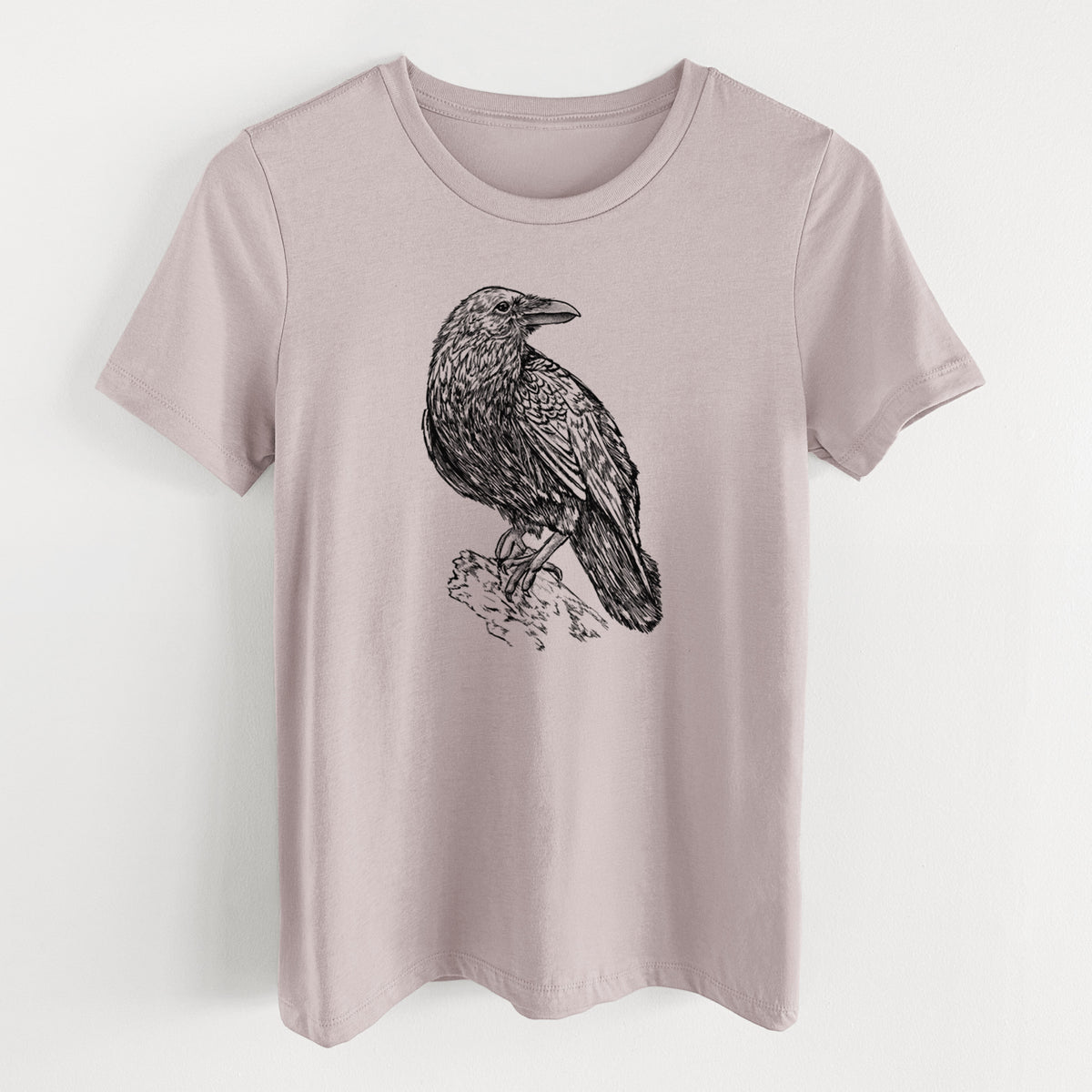 Pink gravel women's relaxed fit cotton t-shirt laid flat, printed with a detailed black ink sketch of a common raven perched on a rock.
