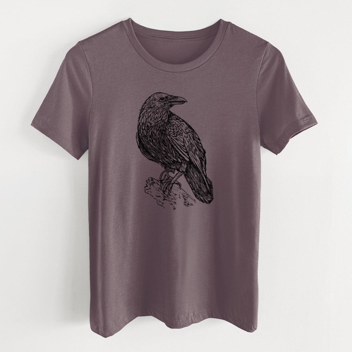 Purple storm women's relaxed fit cotton t-shirt laid flat, printed with a detailed black ink sketch of a common raven perched on a rock.