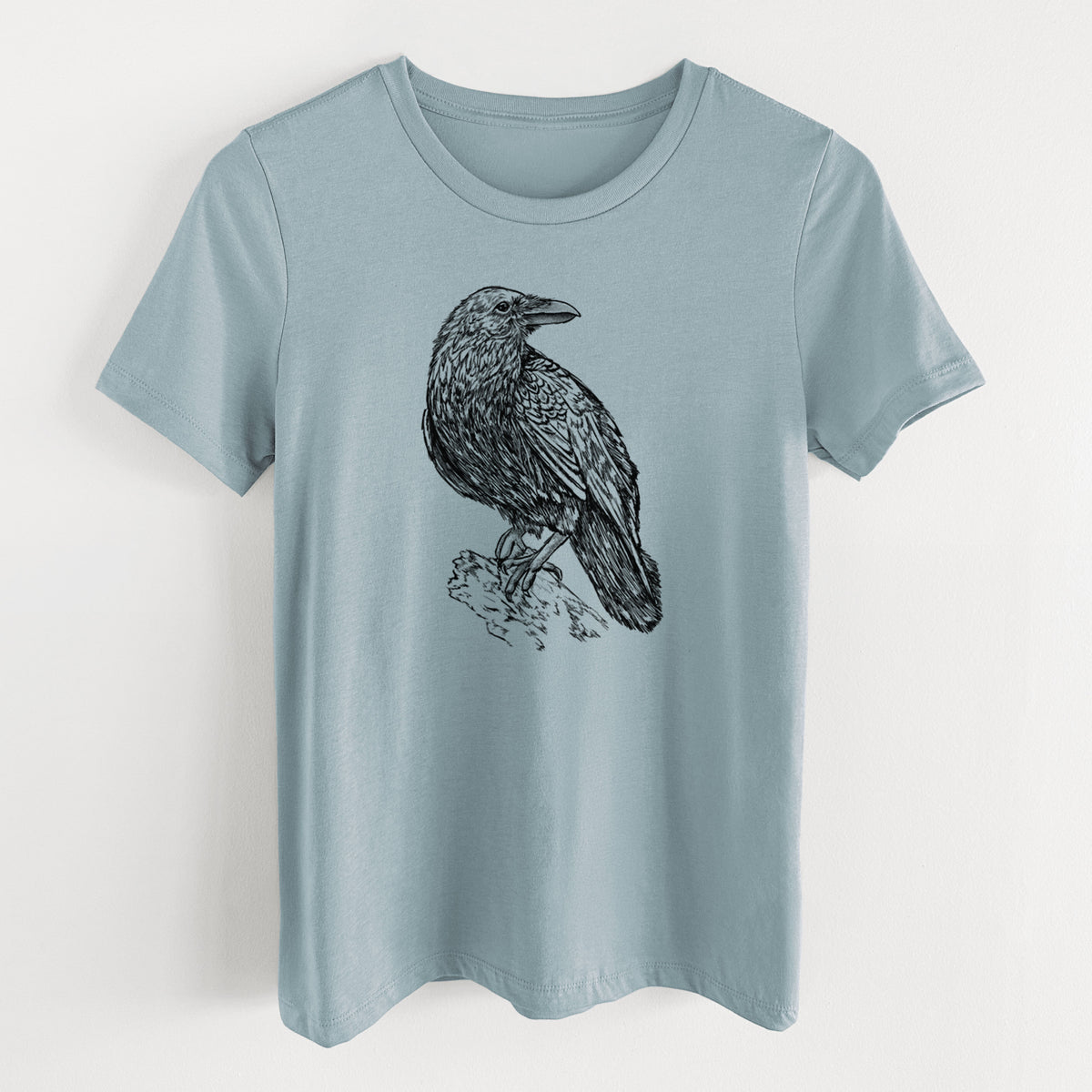 Vintage denim women's relaxed fit cotton t-shirt laid flat, printed with a detailed black ink sketch of a common raven perched on a rock.