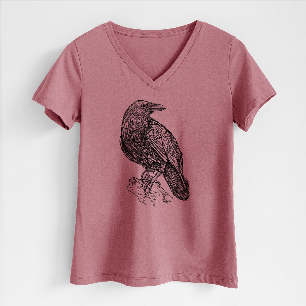 Mauve pink women's relaxed fit cotton V-neck t-shirt laid flat, printed with a detailed black ink sketch of a common raven perched on a rock.