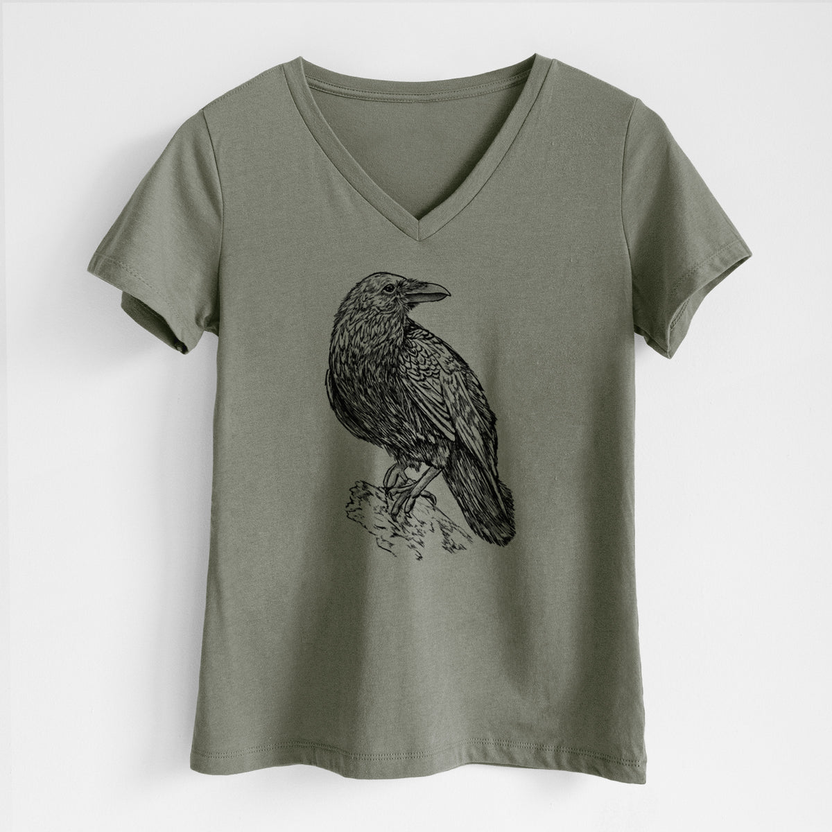 Military green women's relaxed fit cotton V-neck t-shirt laid flat, printed with a detailed black ink sketch of a common raven perched on a rock.