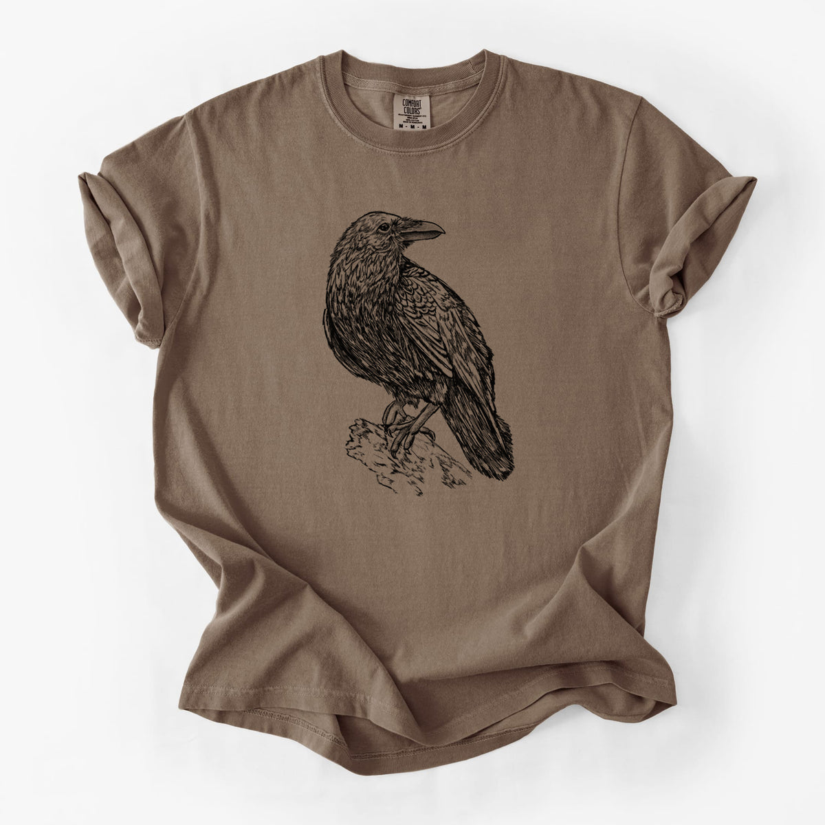 Espresso brown Comfort Colors t-shirt laid flat, printed with a detailed black ink sketch of a common raven perched on a rock.
