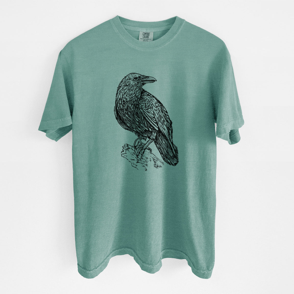 Reef green Comfort Colors t-shirt laid flat, printed with a detailed black ink sketch of a common raven perched on a rock.