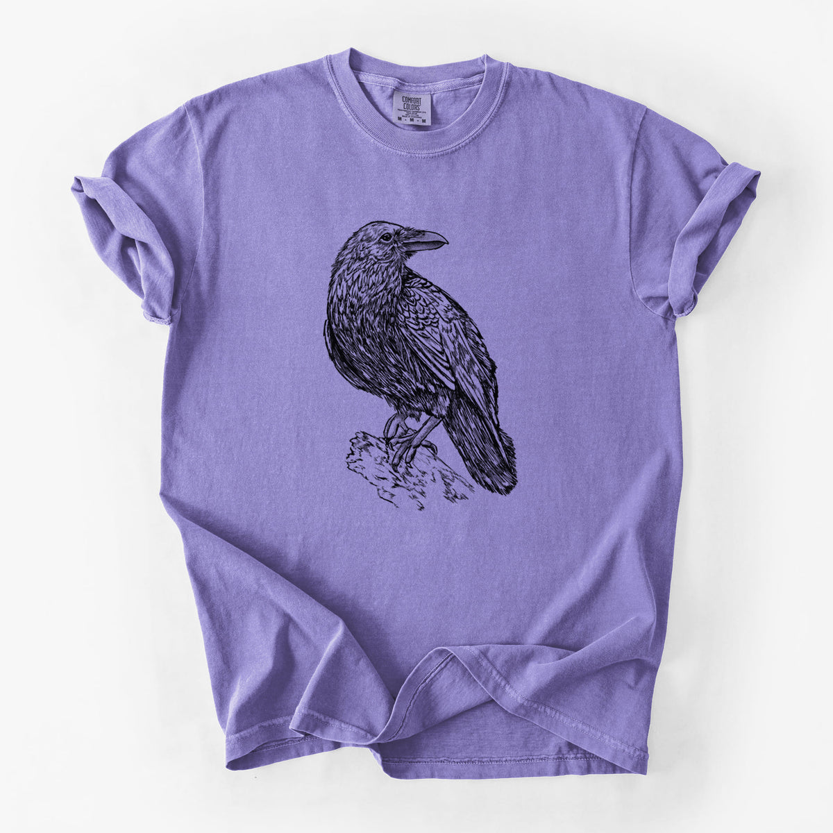 Violet purple Comfort Colors t-shirt laid flat, printed with a detailed black ink sketch of a common raven perched on a rock.