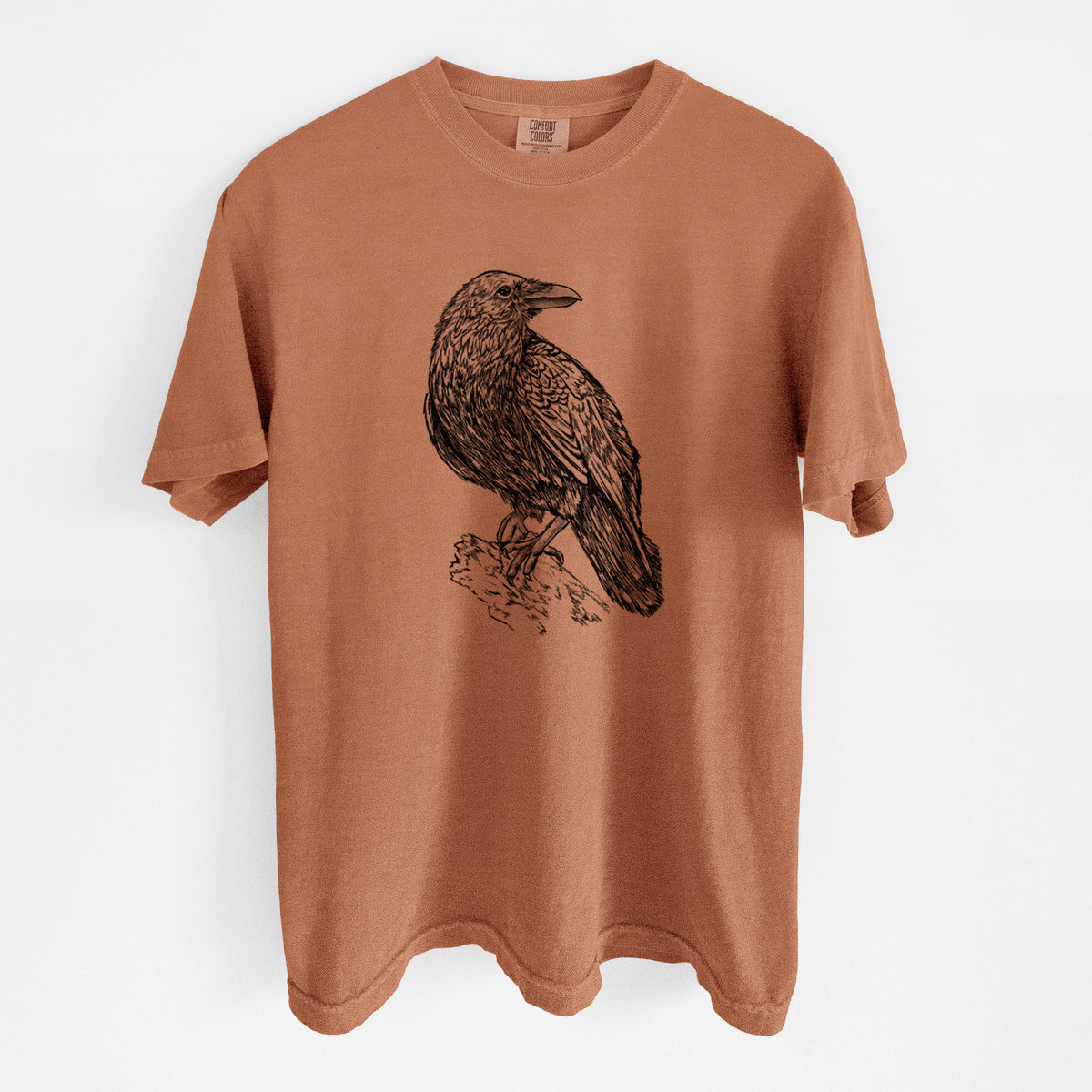 Yam burnt orange Comfort Colors t-shirt laid flat, printed with a detailed black ink sketch of a common raven perched on a rock.