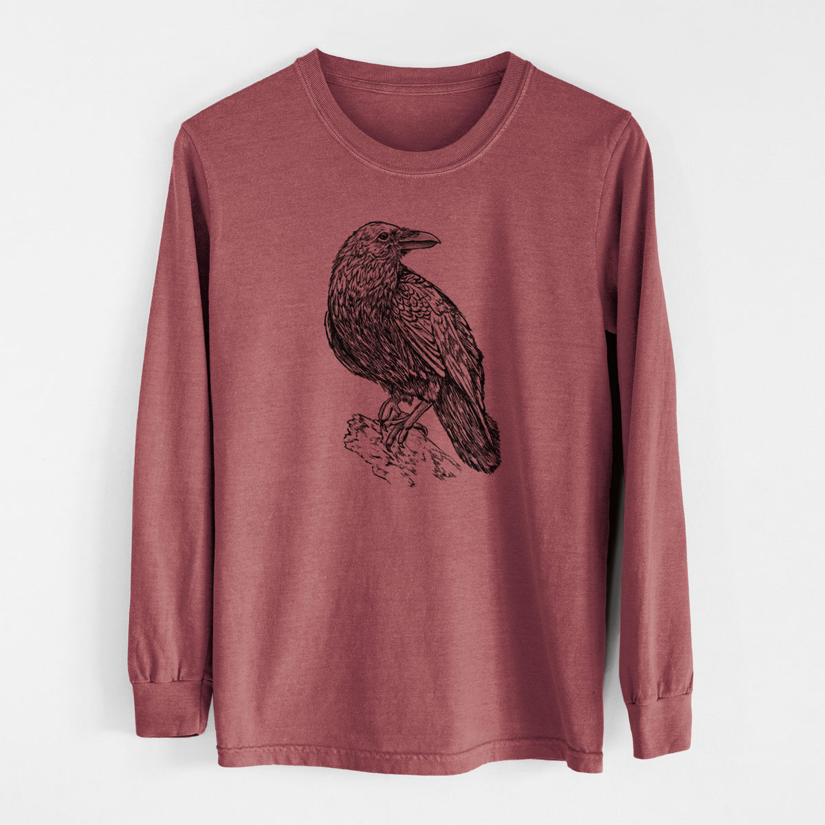 Brick red Comfort Colors long sleeve shirt laid flat, printed with a detailed black ink sketch of a common raven perched on a rock.