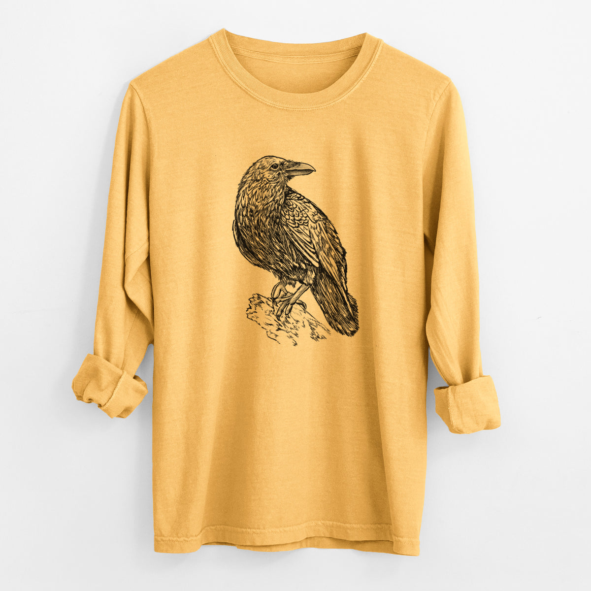 Golden wheat yellow Comfort Colors long sleeve shirt laid flat with the cuffs rolled, printed with a detailed black ink sketch of a common raven perched on a rock.