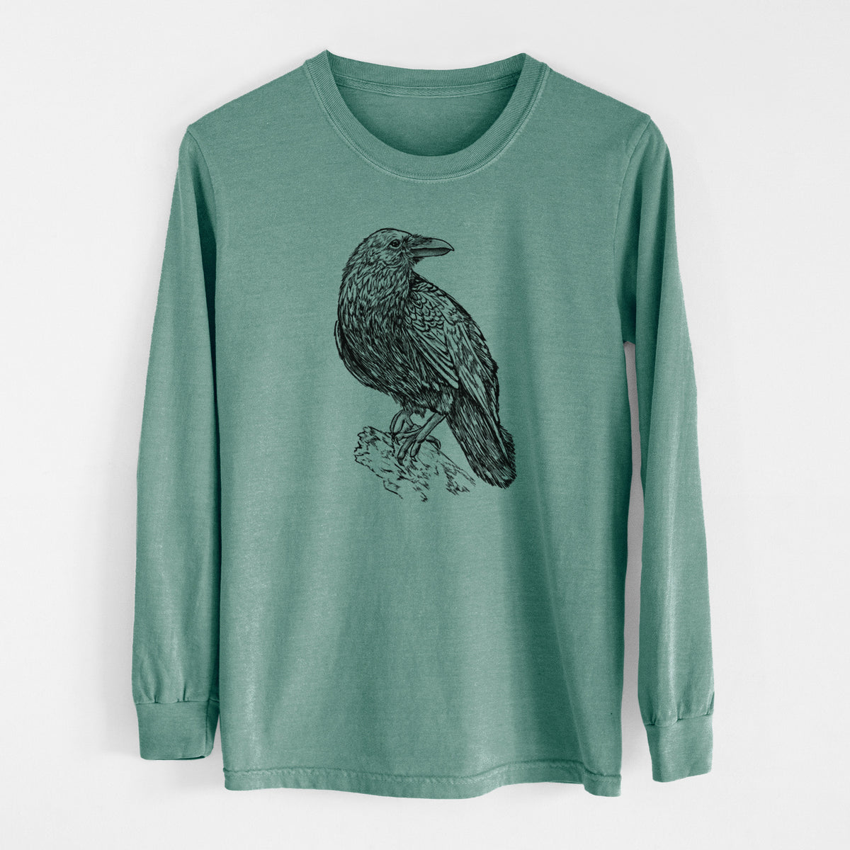 Pine green Comfort Colors long sleeve shirt laid flat, printed with a detailed black ink sketch of a common raven perched on a rock.