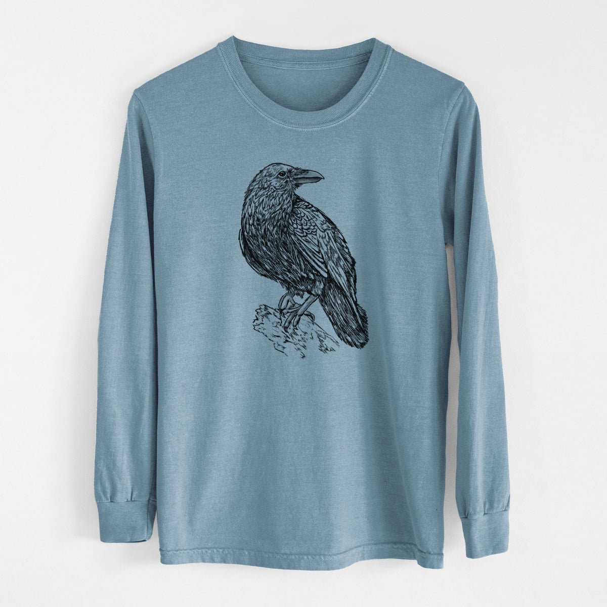 Steel blue Comfort Colors long sleeve shirt laid flat, printed with a detailed black ink sketch of a common raven perched on a rock.