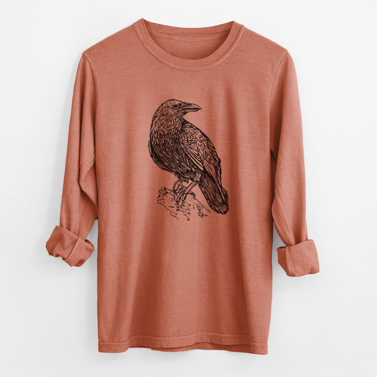 Yam burnt orange Comfort Colors long sleeve shirt laid flat with the cuffs rolled, printed with a detailed black ink sketch of a common raven perched on a rock.