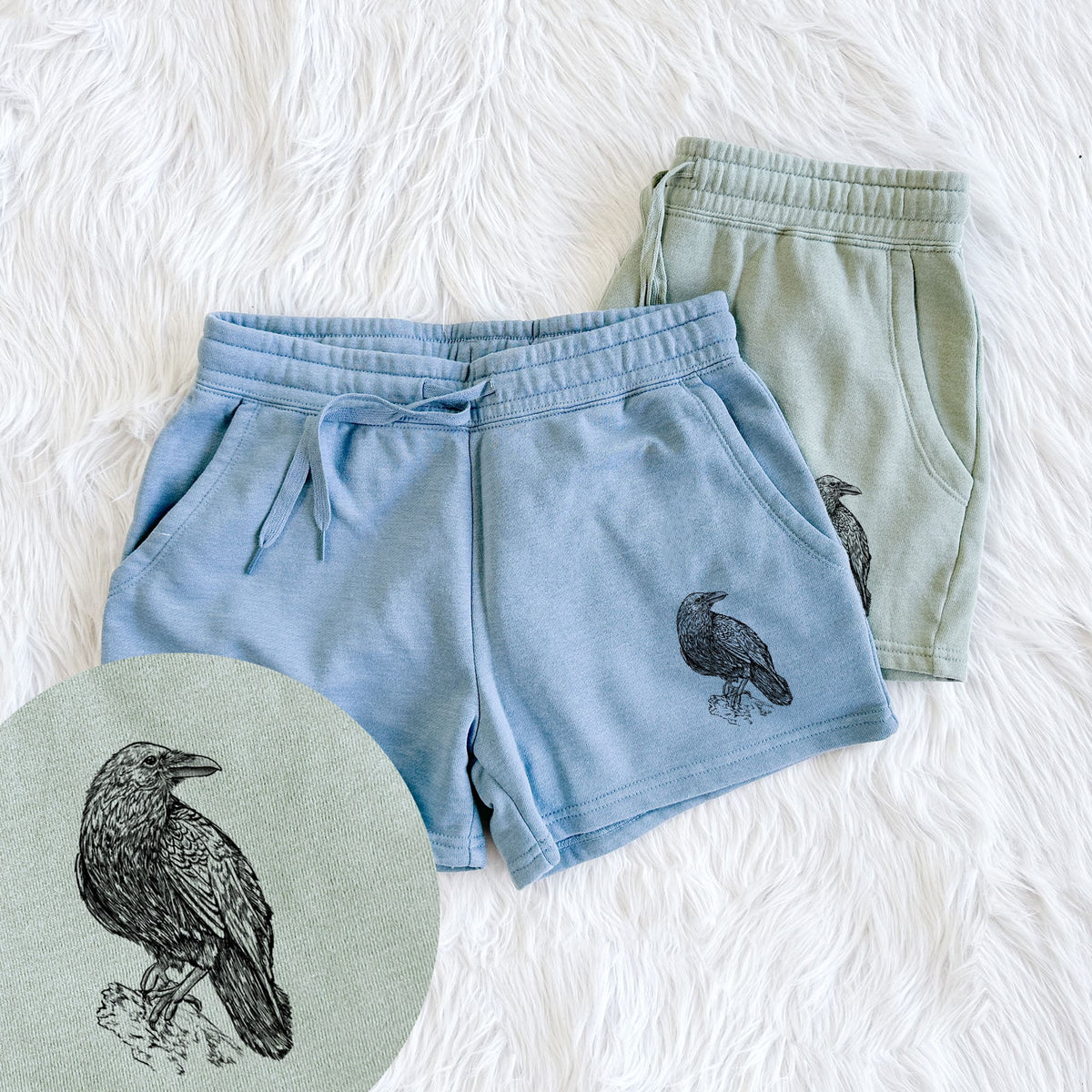 Two pairs of Cali Wave shorts in different colors printed with a detailed black ink sketch of a common raven perched on a rock, with a close-up of the print.