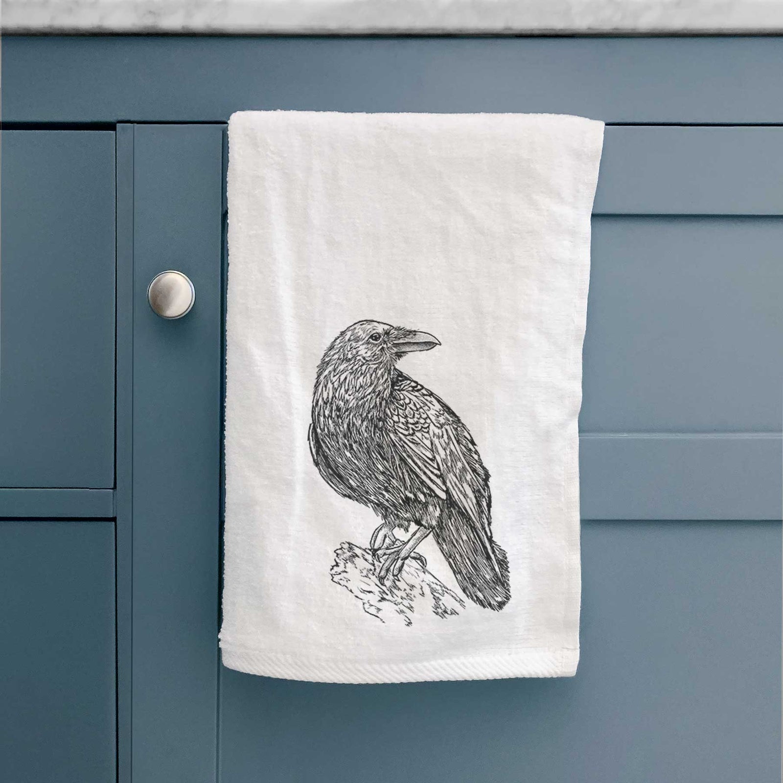 White hand towel printed with a detailed black ink sketch of a common raven perched on a rock.
