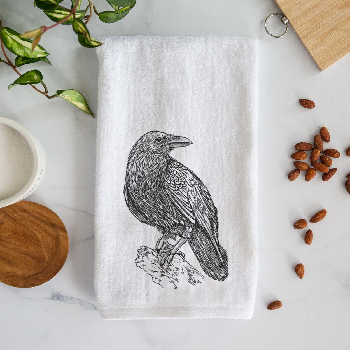 White hand towel printed with a detailed black ink sketch of a common raven perched on a rock.