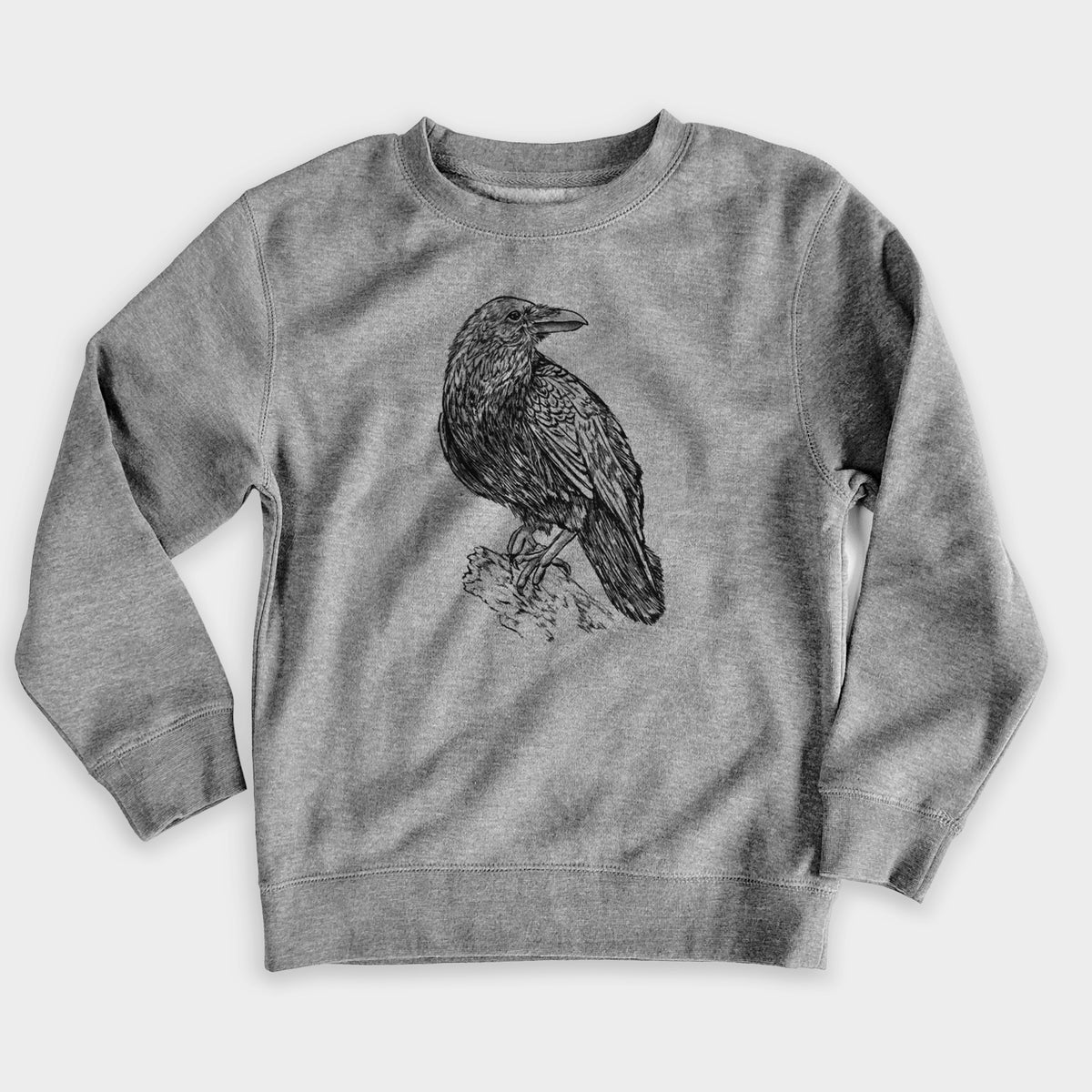 Nickel grey youth crewneck sweatshirt laid flat, printed with a detailed black ink sketch of a common raven perched on a rock.