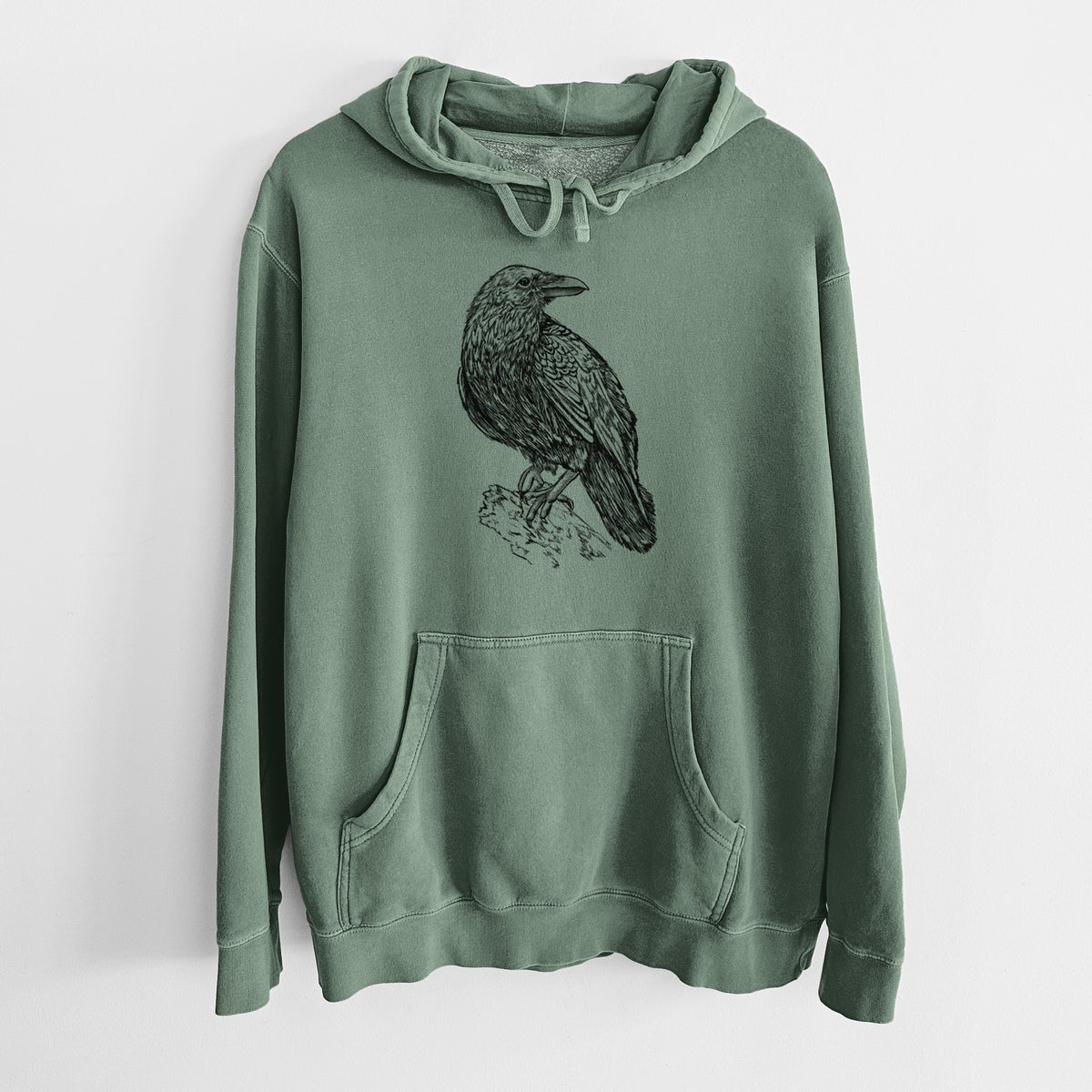 Alpine green pigment dyed hoodie laid flat, printed with a detailed black ink sketch of a common raven perched on a rock.