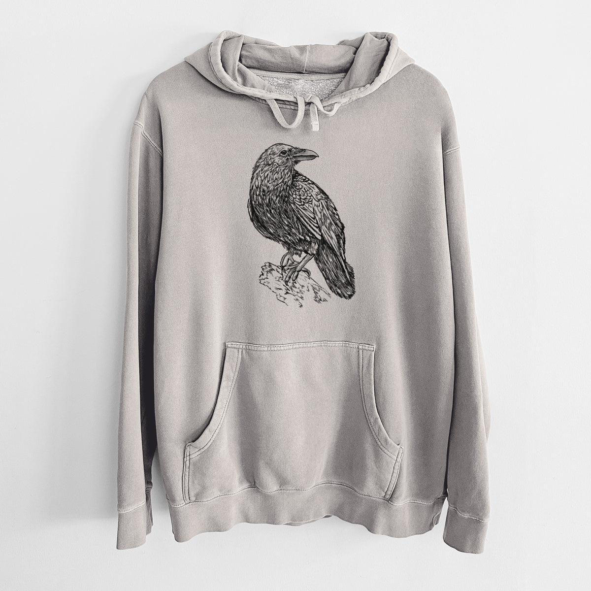 Cement grey pigment dyed hoodie laid flat, printed with a detailed black ink sketch of a common raven perched on a rock.