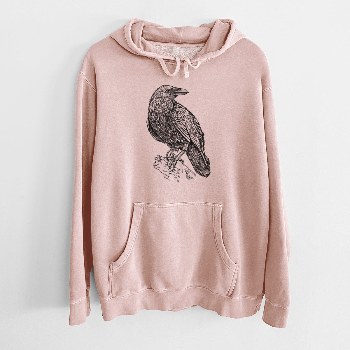 Dusty pink pigment dyed hoodie laid flat, printed with a detailed black ink sketch of a common raven perched on a rock.