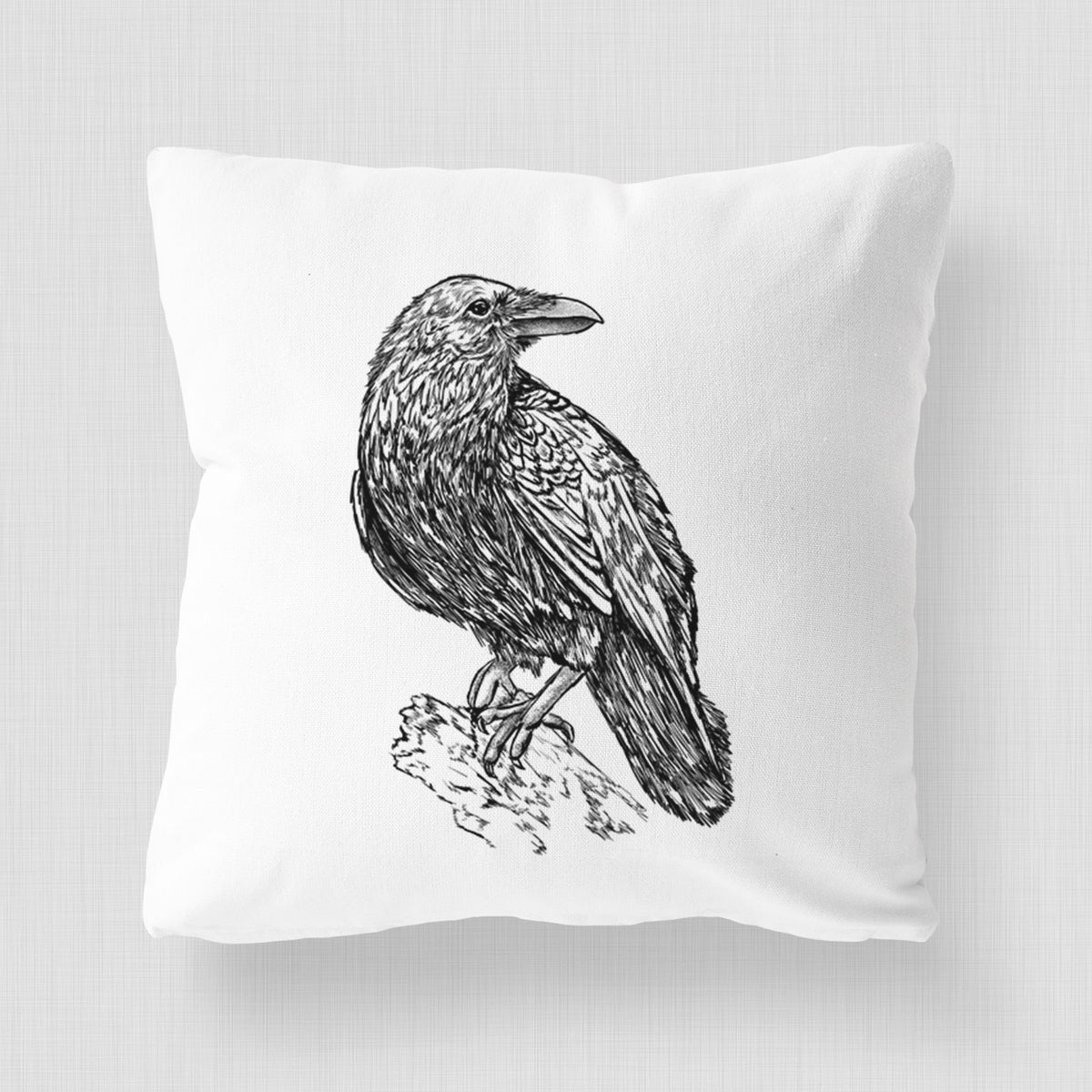 White pillow cover printed with a detailed black ink sketch of a common raven perched on a rock.