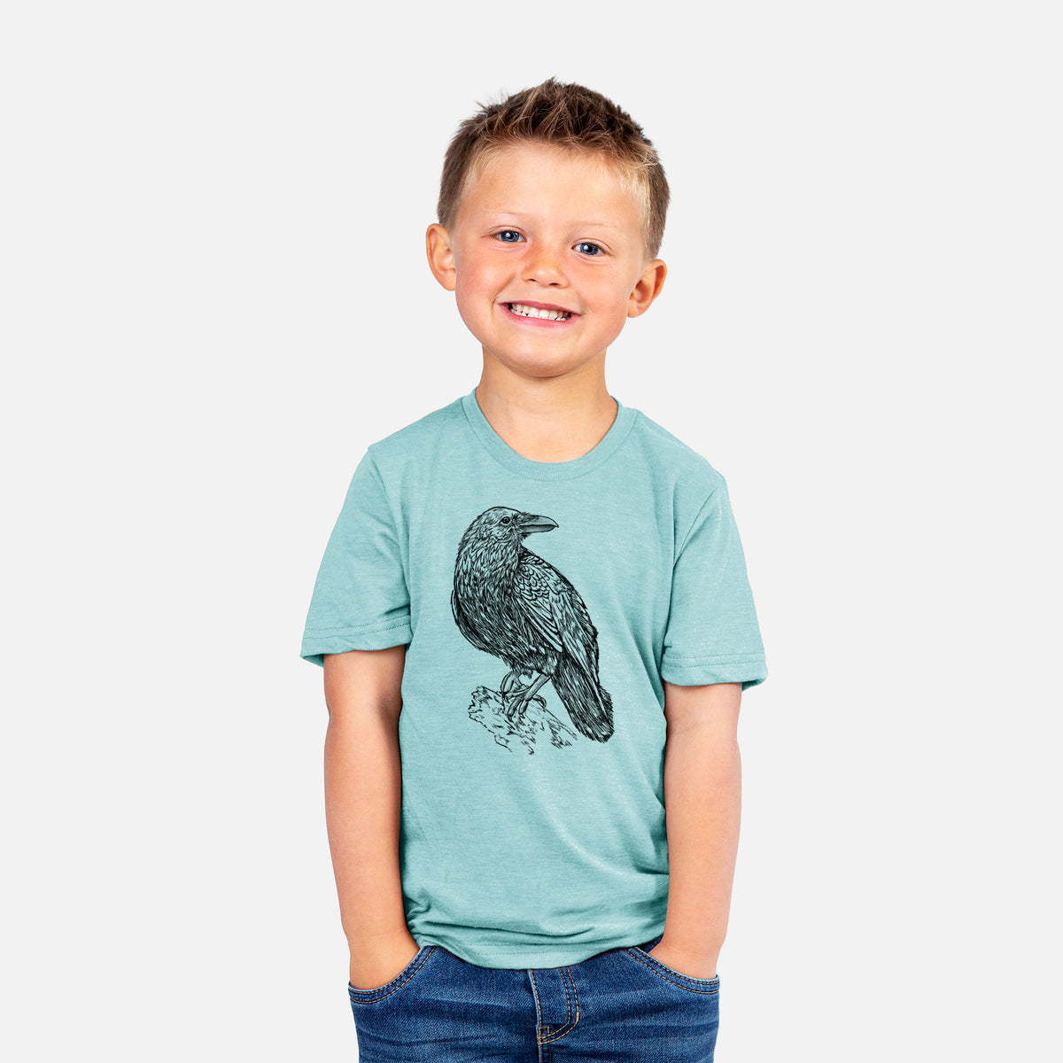 Smiling boy wearing a youth t-shirt printed with a detailed black ink sketch of a common raven perched on a rock.