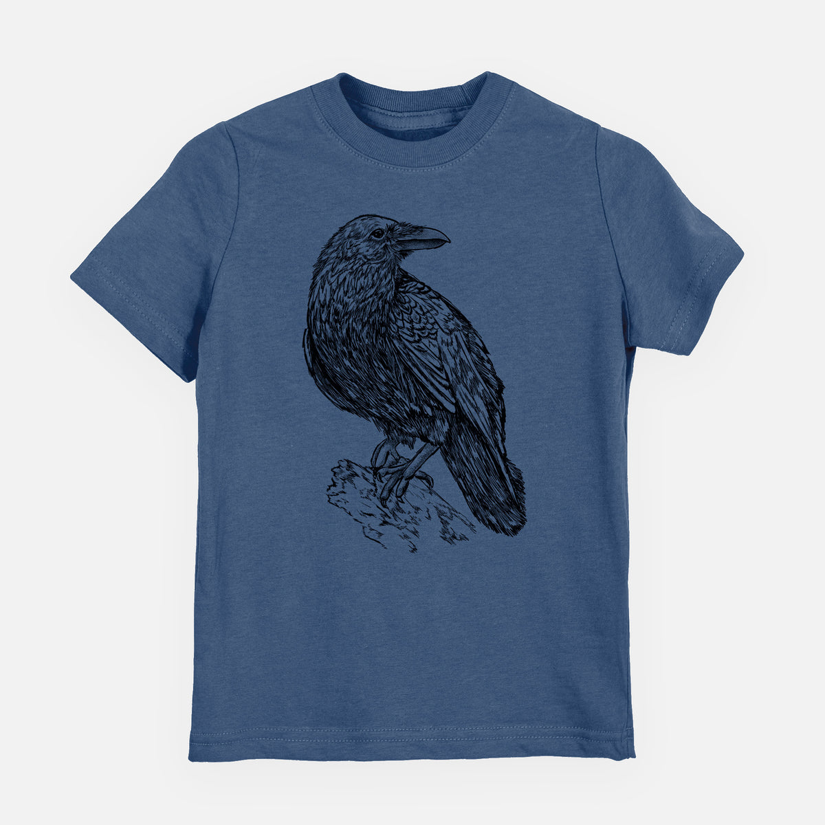 Indigo blue youth t-shirt laid flat, printed with a detailed black ink sketch of a common raven perched on a rock.