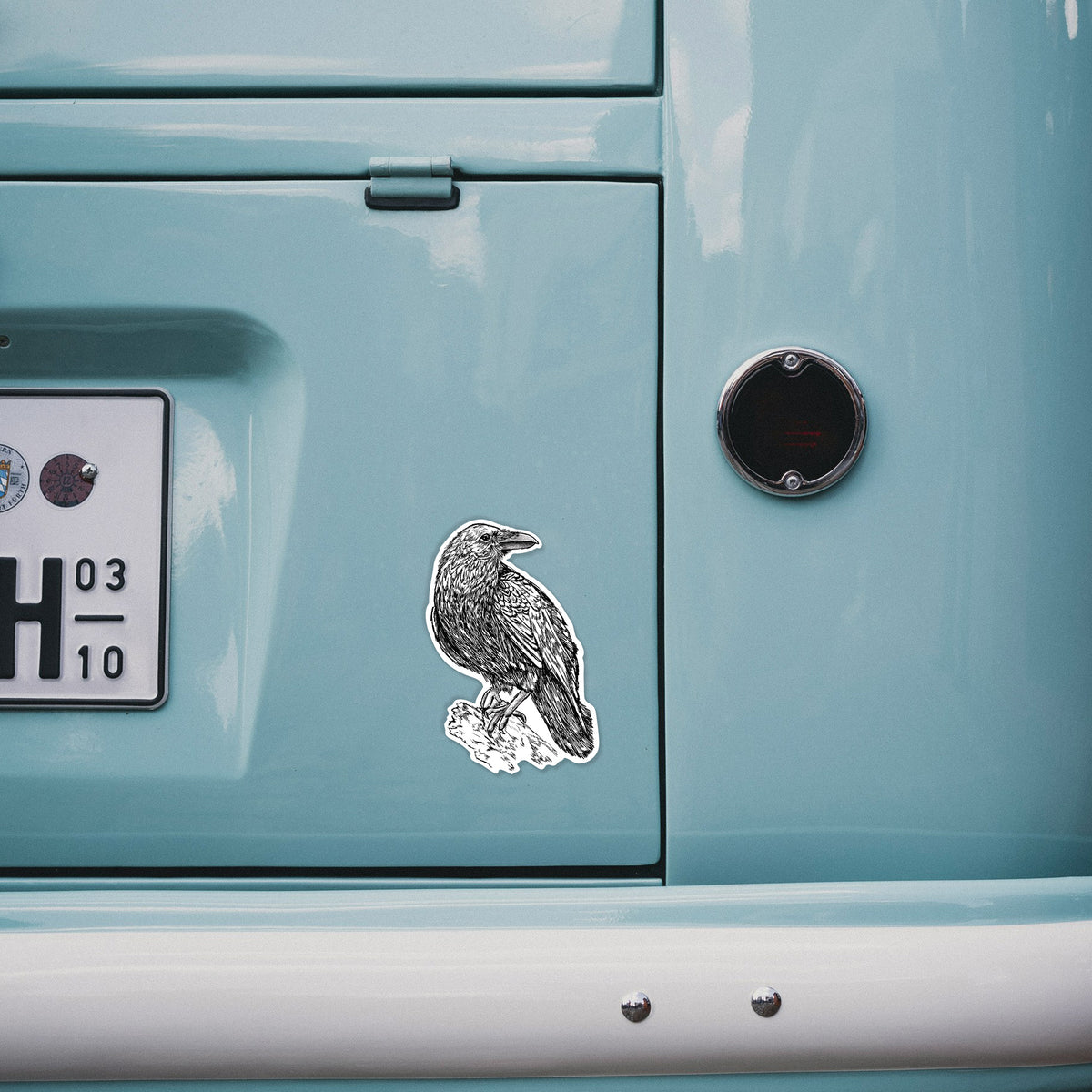 4 inch vinyl decal of a detailed black ink sketch of a common raven perched on a rock on the back of a van.