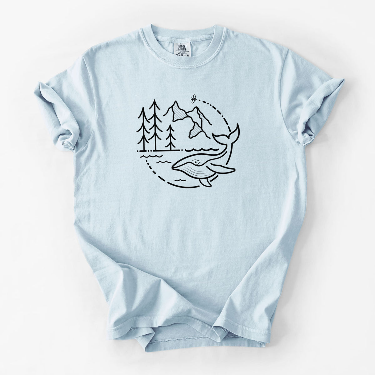 Chambray blue Comfort Colors t-shirt laid flat, printed with a black line art circle connecting a mountain range, pine trees, a bee and a whale swimming in ocean waves.