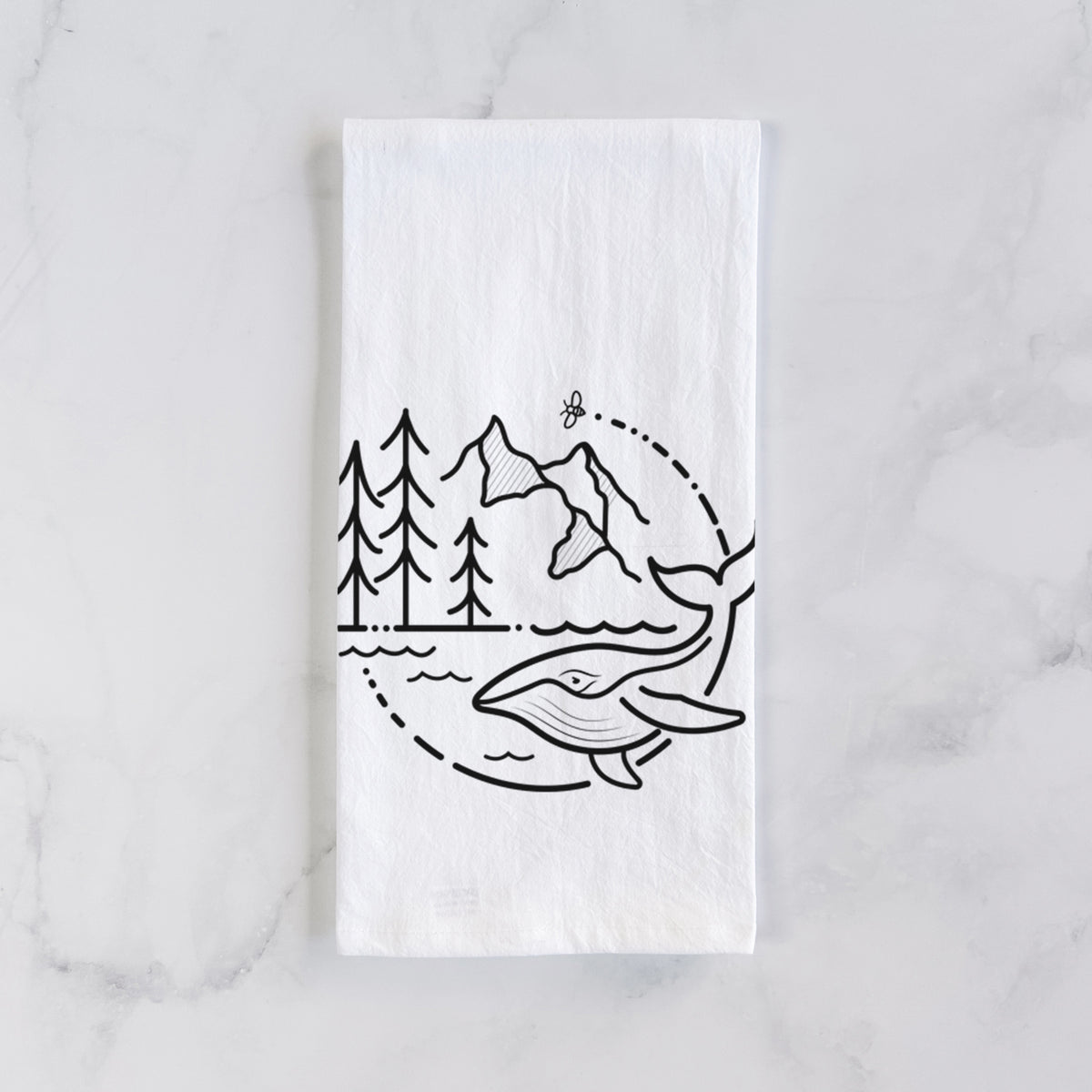 White cotton tea towel laid flat on marble, printed with a black line art circle connecting a mountain range, pine trees, a bee and a whale swimming in ocean waves.