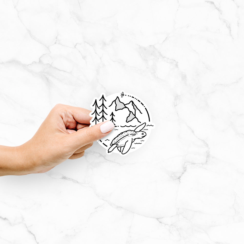 Hand holding a 4 inch vinyl decal of a black line art circle connecting pine trees, mountains, a bee and a Kemp's ridley sea turtle swimming.