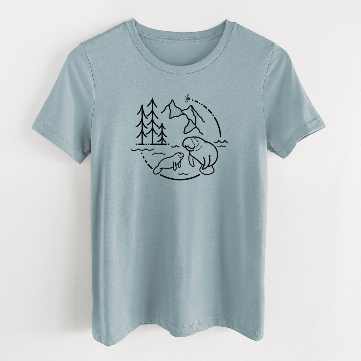 Vintage denim women's relaxed fit cotton t-shirt laid flat, printed with a black line art circle connecting pine trees, mountains, a bee and two manatees swimming in water.