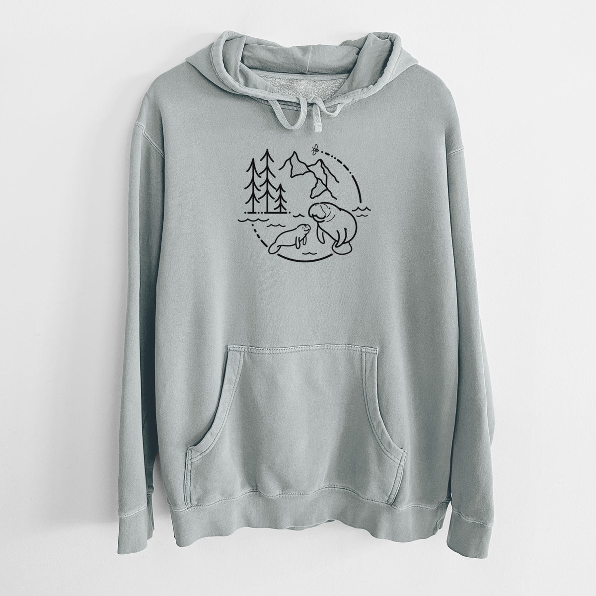 Sage green pigment dyed hoodie laid flat, printed with a black line art circle connecting pine trees, mountains, a bee and two manatees swimming in water.