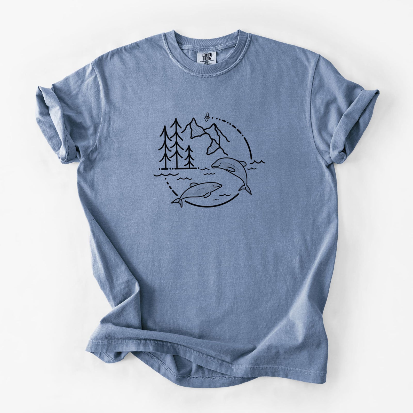 Blue jean Comfort Colors t-shirt laid flat, printed with a black line art circle connecting pine trees, mountains, a bee and two Maui dolphins leaping from the waves.