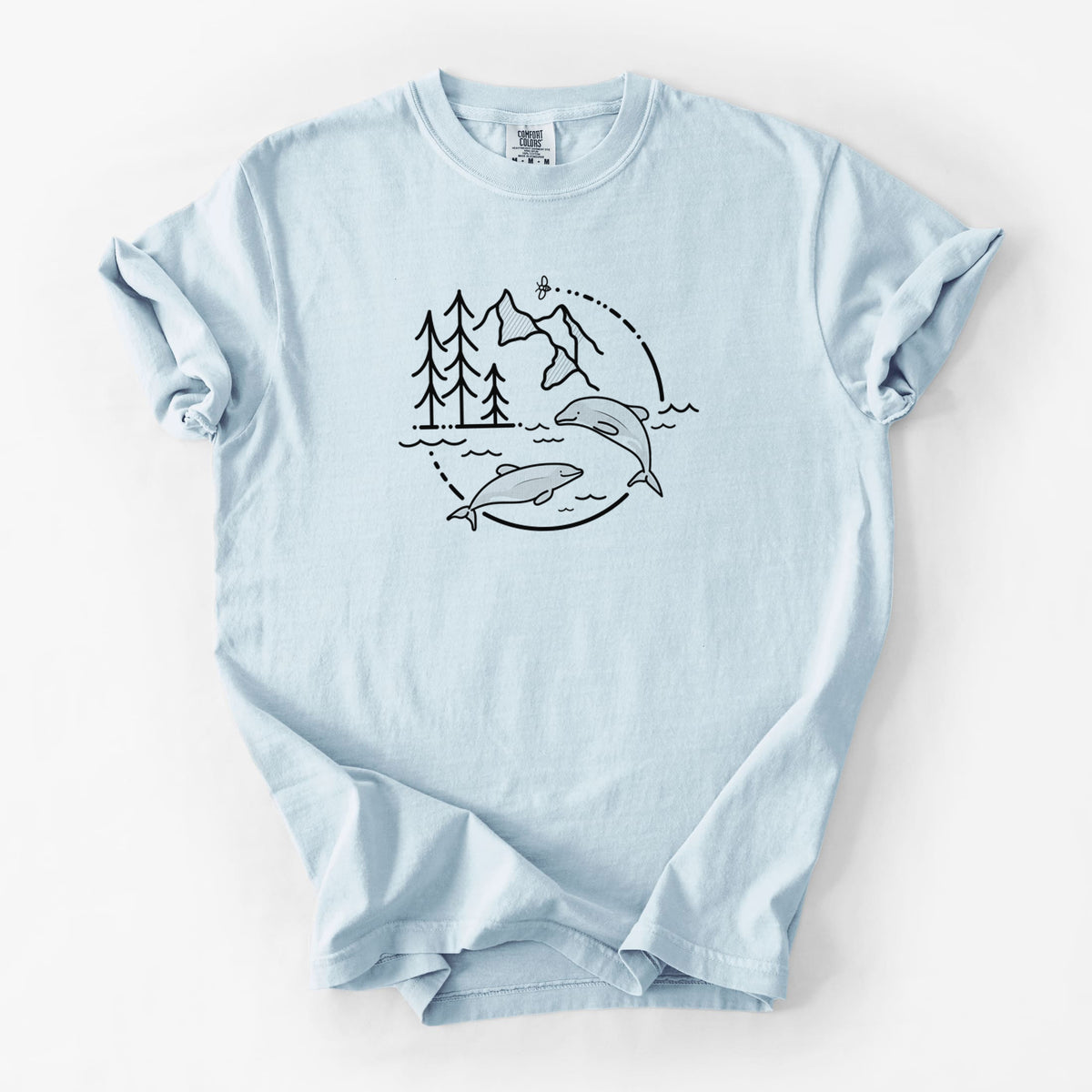 Chambray blue Comfort Colors t-shirt laid flat, printed with a black line art circle connecting pine trees, mountains, a bee and two Maui dolphins leaping from the waves.