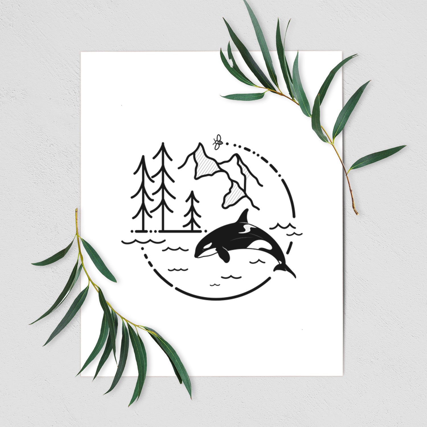Art print of a black line art circle connecting pine trees, mountains, a bee and an orca leaping from ocean waves, shown with eucalyptus leaves.