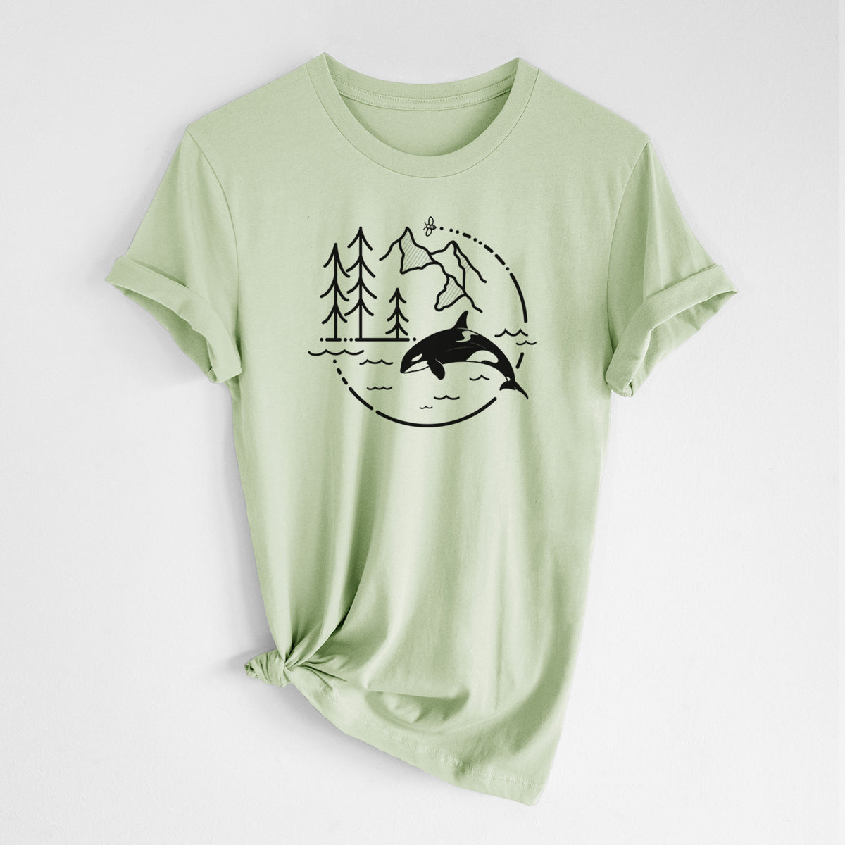 Spring green lightweight cotton t-shirt laid flat with the sleeves rolled, printed with a black line art circle connecting pine trees, mountains, a bee and an orca leaping from ocean waves.
