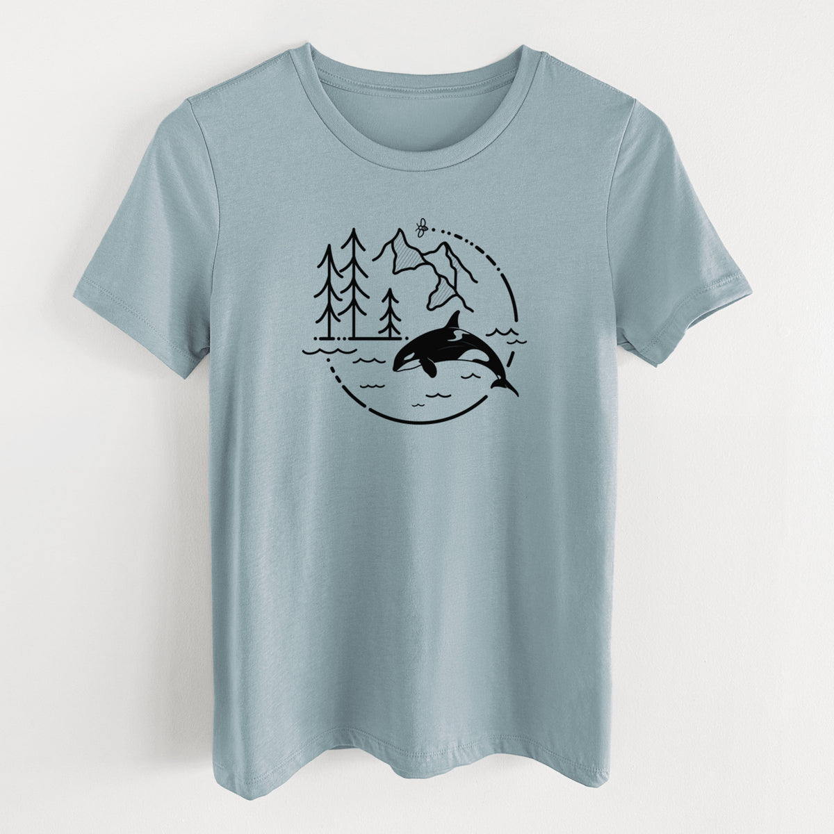Vintage denim women's relaxed fit cotton t-shirt laid flat, printed with a black line art circle connecting pine trees, mountains, a bee and an orca leaping from ocean waves.