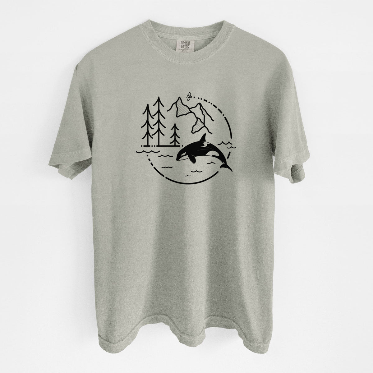 Sandstone beige Comfort Colors t-shirt laid flat, printed with a black line art circle connecting pine trees, mountains, a bee and an orca leaping from ocean waves.